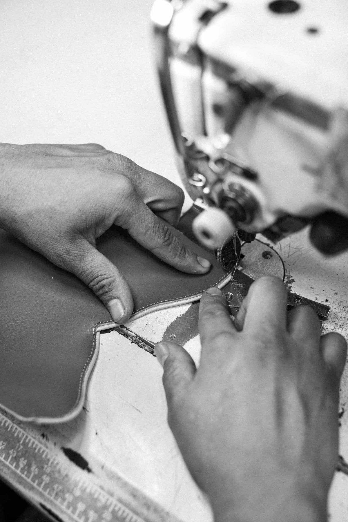 Hands sewing a piece of leather at a machine, in black and white