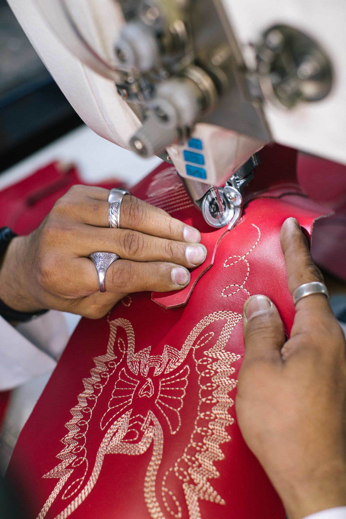 Hands stitching the phoenix embroidery on a red boot shaft
