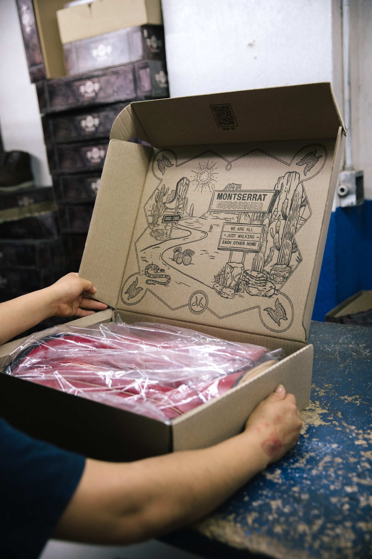 Hands closing a Montserrat Messeguer shipping box with red boots inside