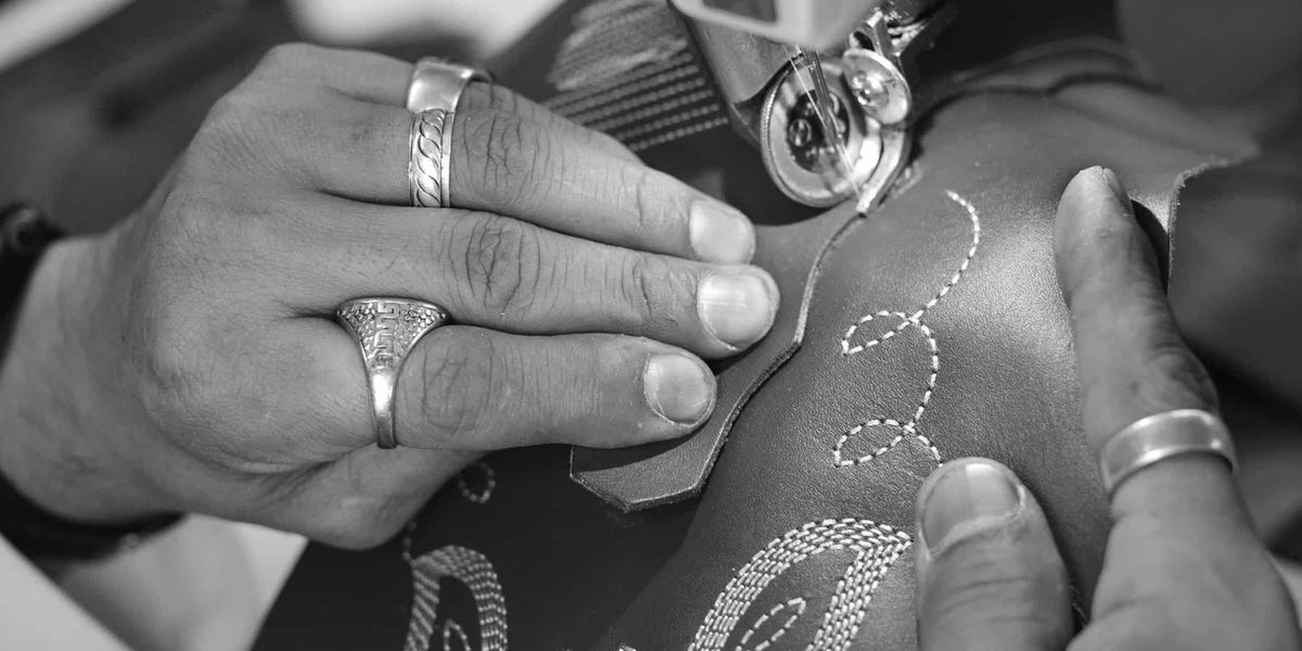 Ringed hands working on a boot's embroidery, in black and white