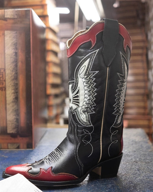 Black cowboy boot with red overlays and white embroidery, in the workshop