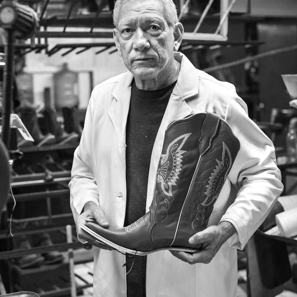 Artisan in a white coat holding a cowboy boot in the workshop, in black and white