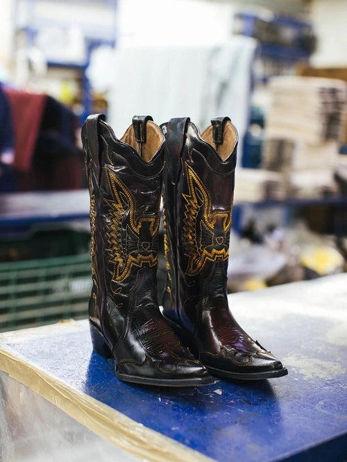 Pair of black cowboy boots with gold embroidery on a workshop table