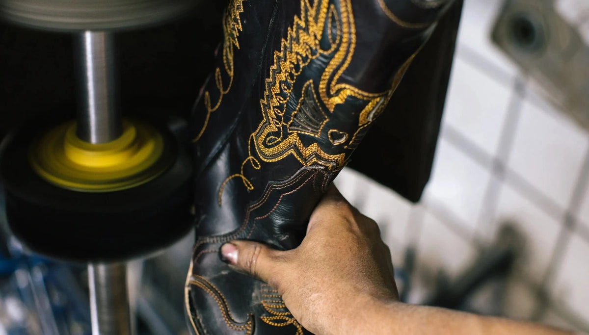 Hands polishing a black boot with gold embroidery