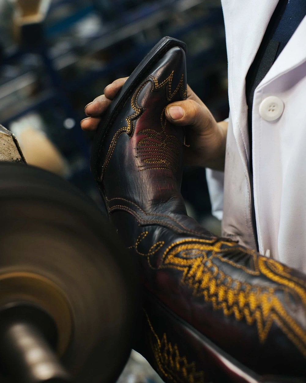 Artisan in a white coat polishing a black and burgundy cowboy boot