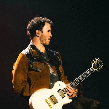 Integrante de los Jonas Brothers tocando la guitarra en concierto, con chamarra de gamuza Montserrat Messeguer