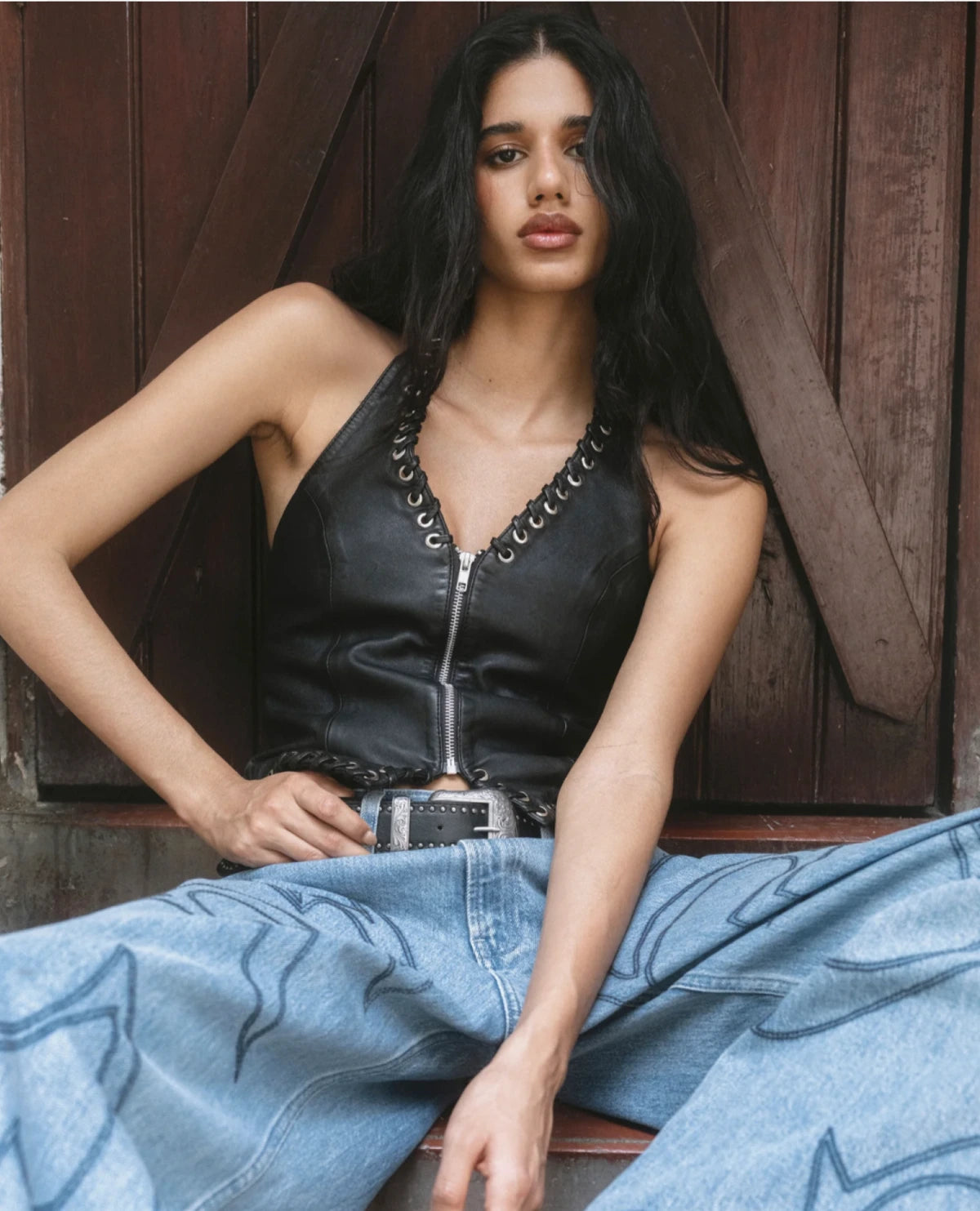Modelo sentada con top de piel negro con ojillos y jeans con motivos western