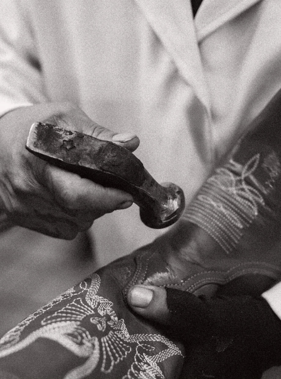 Manos de artesano con un martillo sobre el bordado de una bota, en blanco y negro