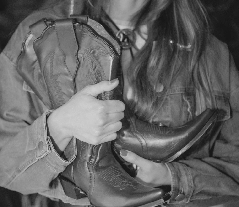 Woman in a denim shirt holding a leather cowboy boot, in black and white