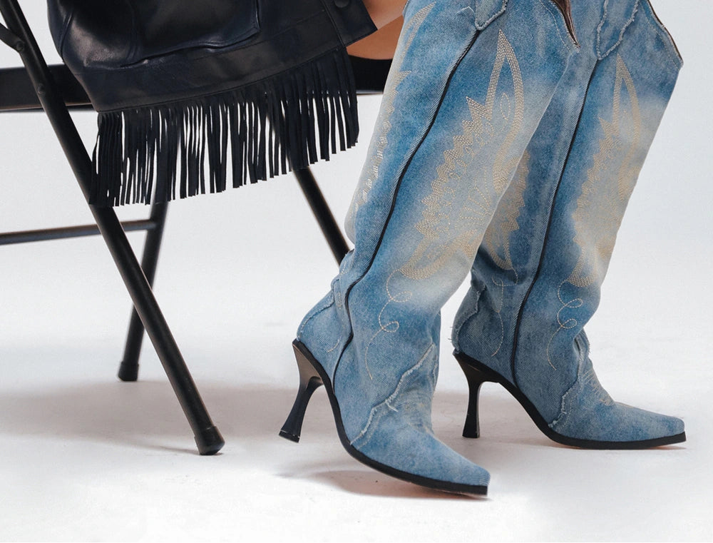 Botas vaqueras de mezclilla deslavada con tacón, junto a una silla plegable con una chamarra de flecos